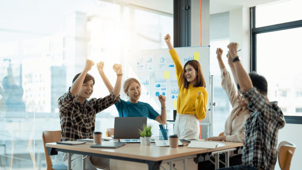 a group of people sitting around a table with their hands in the air