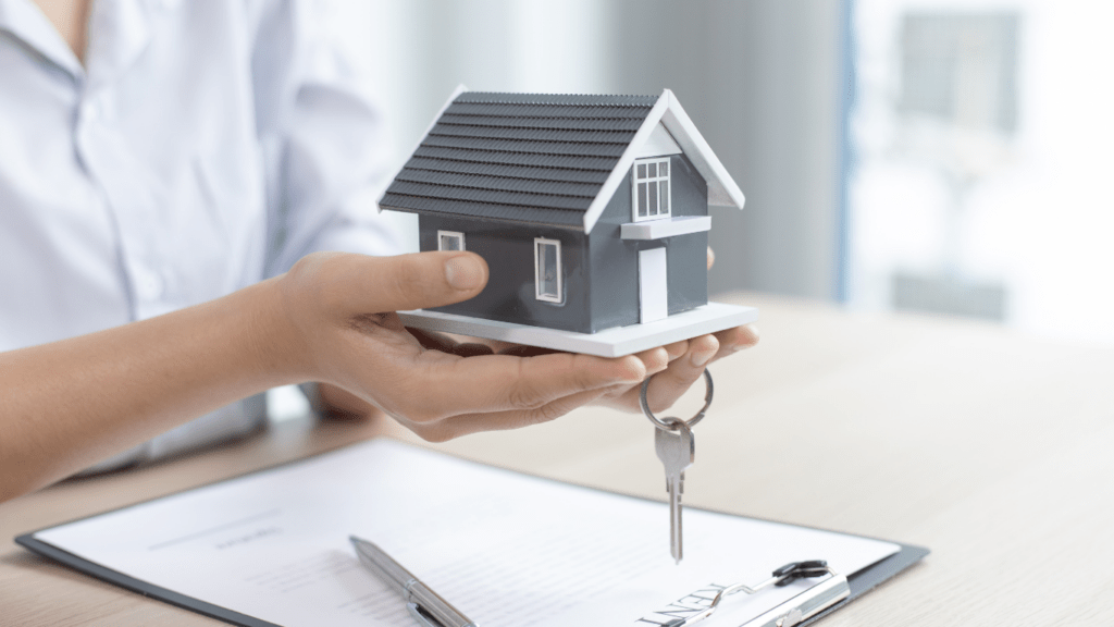 a person holding a house model and keys on a desk