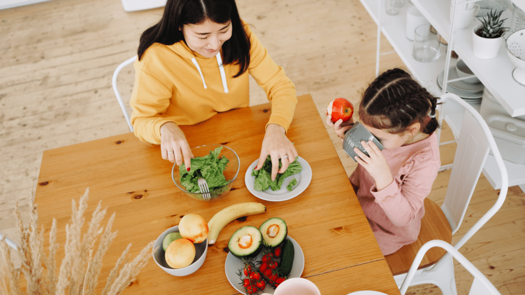 A parent and child are sitting at a table with fruits and vegetables