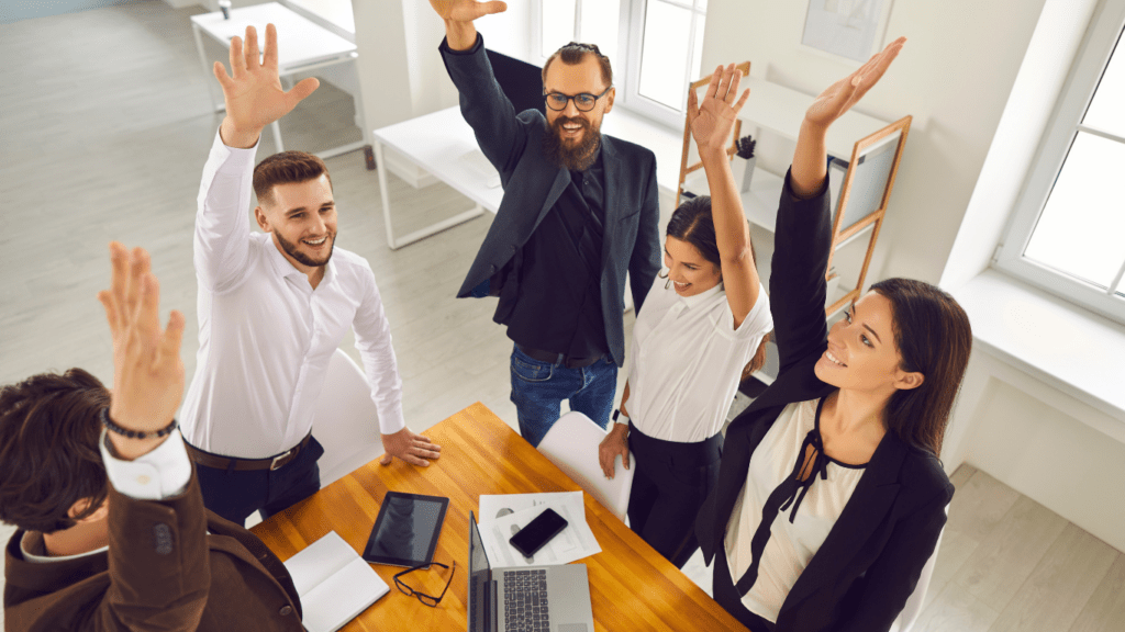 a group of people sitting around a table with their hands in the air